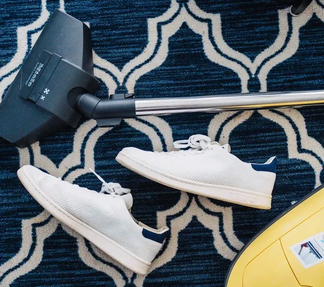 Dammsugare på en mönstrad matta bredvid ett par vita sneakers